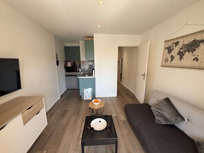 Ein gemütlicher, kleiner Wohnbereich mit einer Couch, einem Tisch mit Schüssel und Teller, einem Fernseher und einer Küchenzeile im Hintergrund.