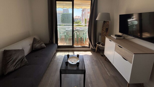 Ein modernes Wohnzimmer mit Sofa, Couchtisch, Fernseher und einem Balkon mit Gartenmöbeln.