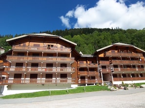 Een meerlaags houten gebouw met balkons, waarschijnlijk een hotel of lodge, met een bebost berglandschap op de achtergrond.