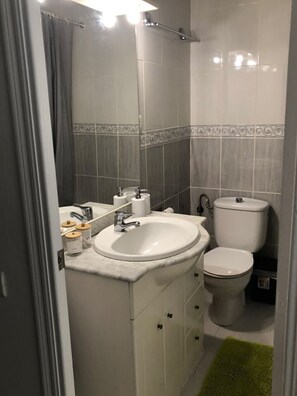 A bathroom with a white sink, toilet, and vanity with cabinets. - Roger Economic Study (Cambrils)