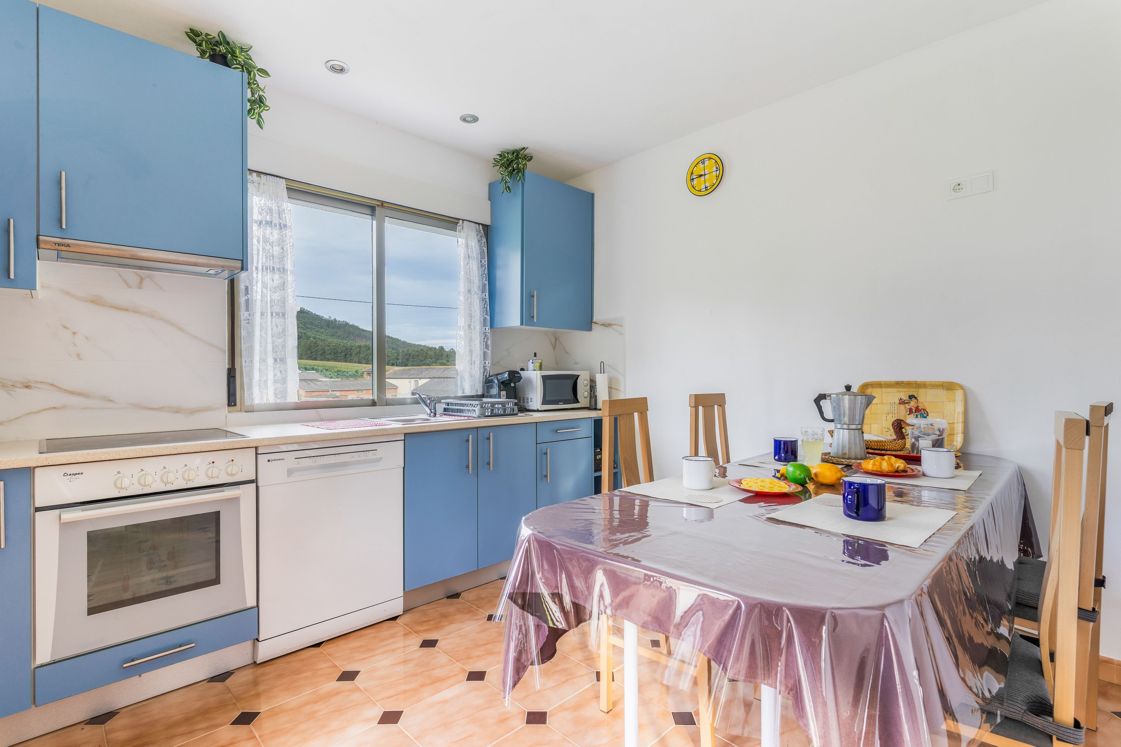 A kitchen with blue cabinets, a white dishwasher, a stove, and a window with a view of greenery.