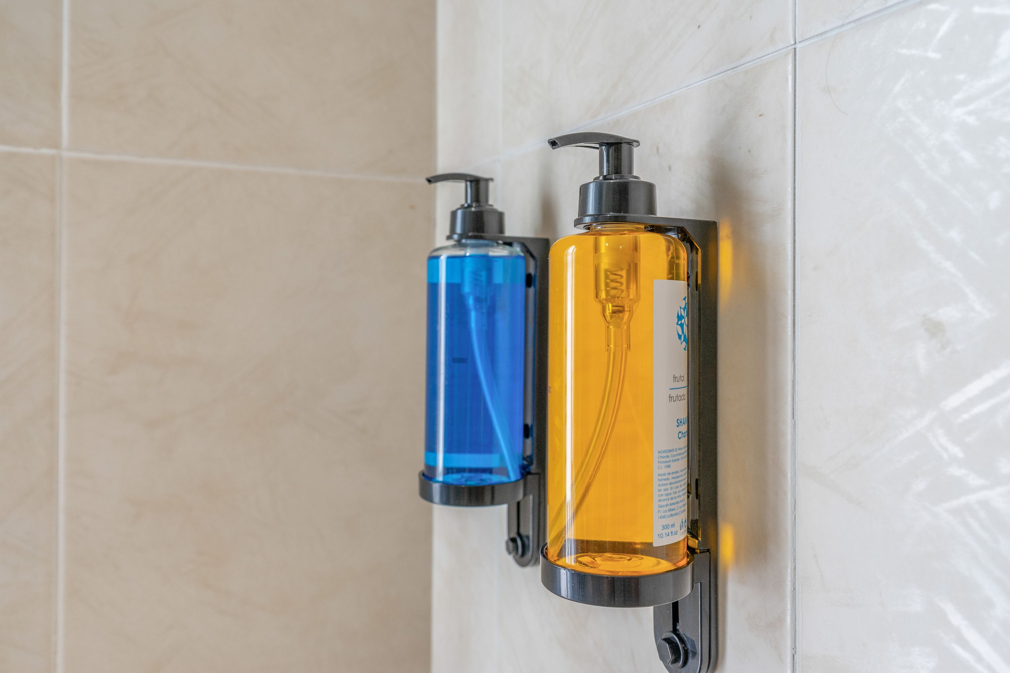 Two bottles of liquid soap mounted on a tiled wall.