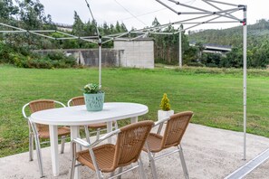 An outdoor patio with a round table and four wicker chairs, a potted plant, and a small tree.