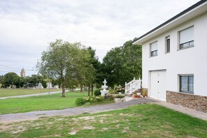 Una proprietà residenziale con facciata bianca, fondazione in pietra, giardino antistante con fontana bianca e cielo sereno.