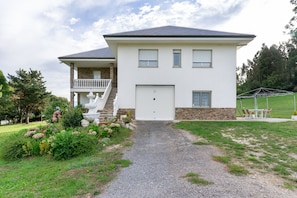A two-story house with a front porch, a stone foundation, and a gravel driveway.