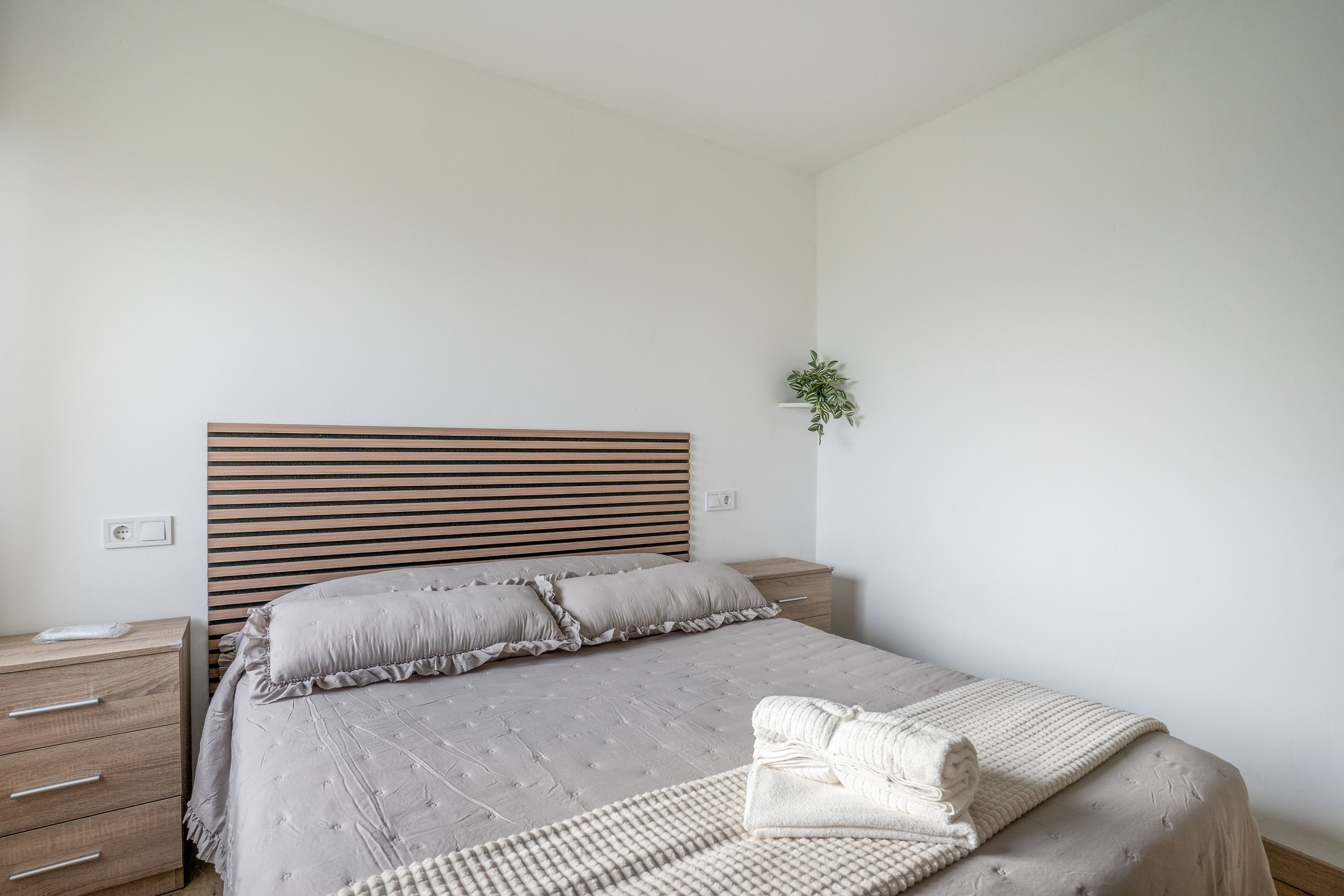 A bedroom with a bed, bedside tables, a wall-mounted plant, and a power outlet.