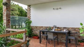 Een terras buiten met een tafel en stoelen, omgeven door potplanten en een stenen muur.