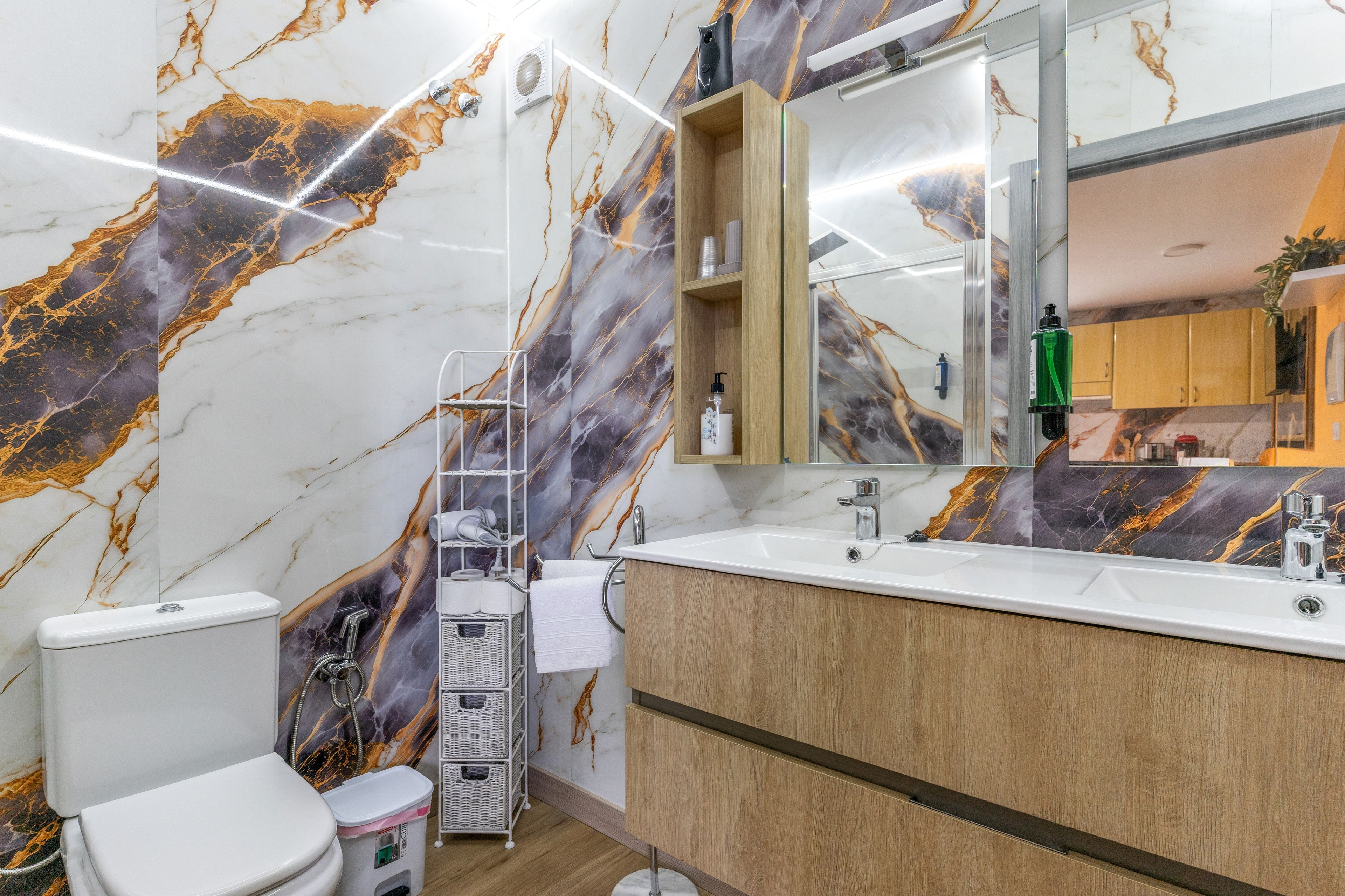 Un baño moderno con salpicadero de mármol, tocador de madera, un espejo grande y un inodoro.
