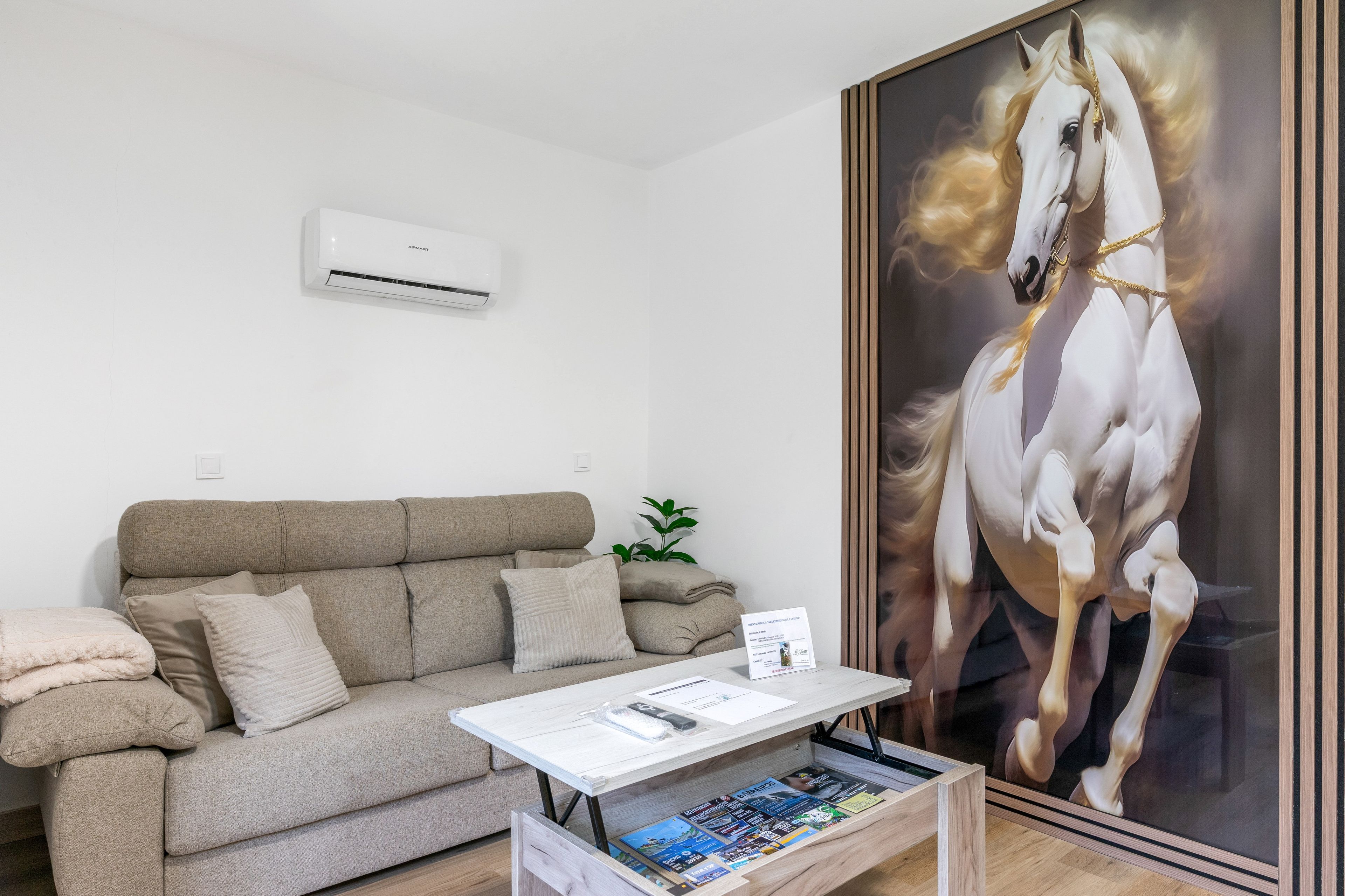 Een kamer met een beige bank, een witte salontafel en een groot schilderij van een witte paard.