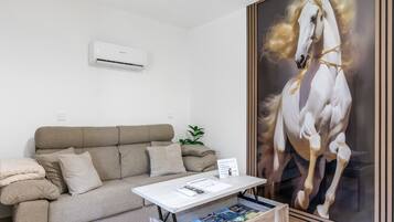 Een kamer met een beige bank, een witte salontafel en een groot schilderij van een witte paard.