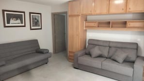 A living room with two grey sofas, wooden cabinets, and two framed pictures on the wall.