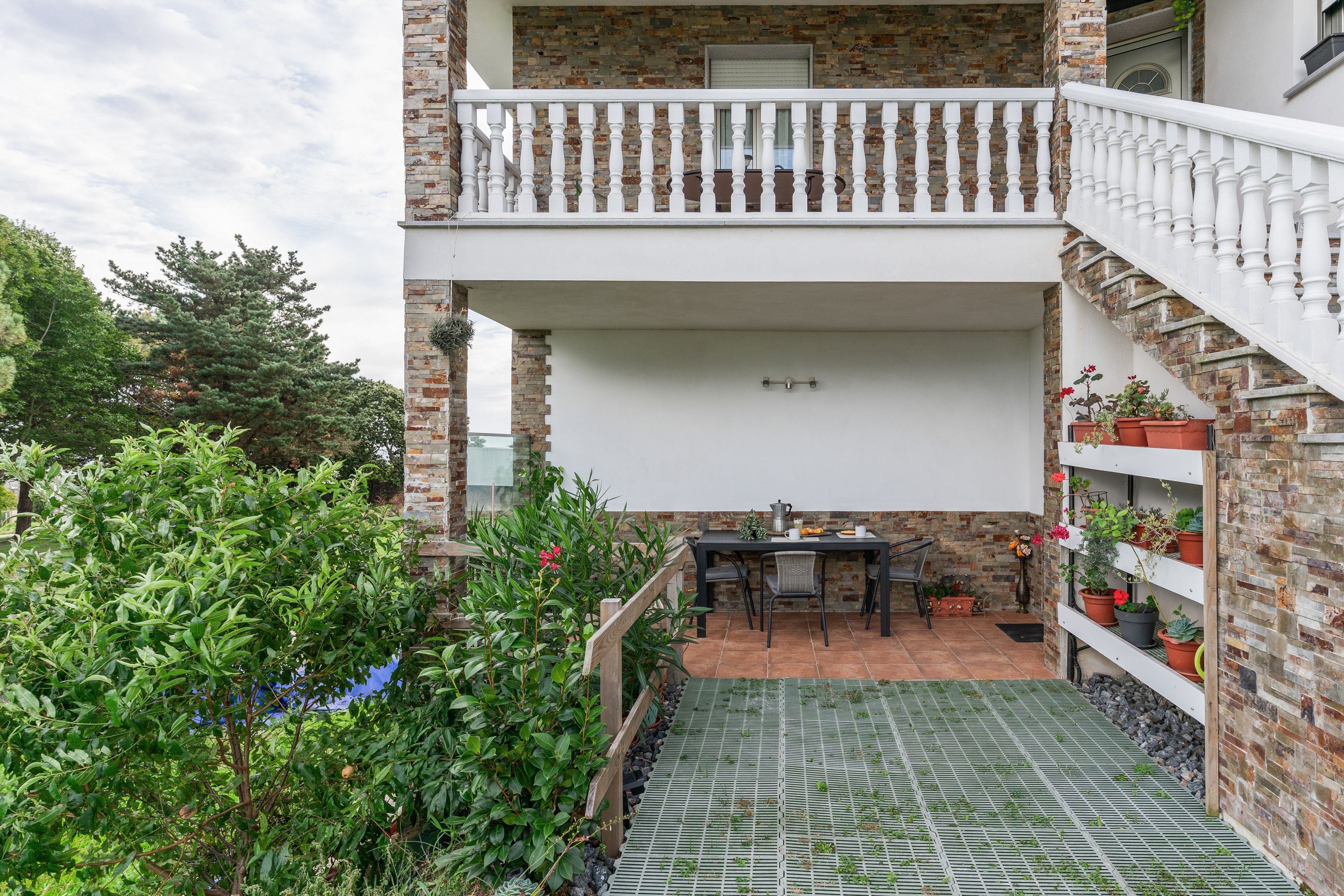 Une terrasse extérieure couverte, avec une table et des chaises, entourée de plantes en pot et d’un mur de briques.