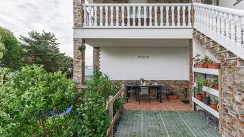 Une terrasse extérieure couverte, avec une table et des chaises, entourée de plantes en pot et d’un mur de briques.