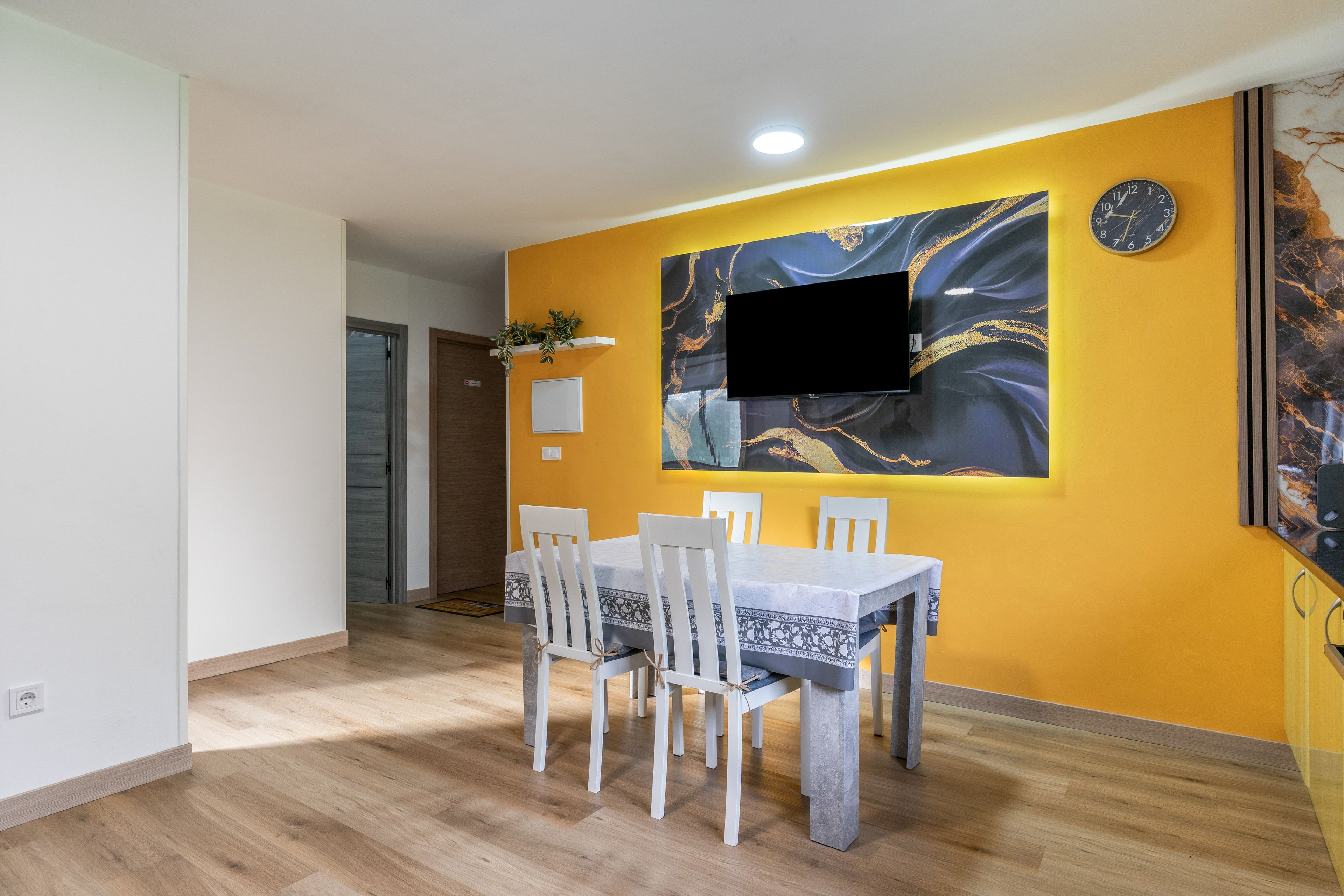 Ein Essbereich mit Tisch und Stühlen, einem an der Wand befestigten Flachbildfernseher und einer Tür zu einem anderen Raum.