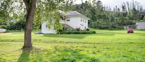 Une maison blanche dotée d’un balcon, entourée d’un champ verdoyant et d’arbres.