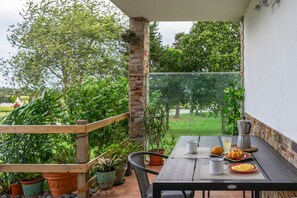 A patio with a table set for breakfast, surrounded by potted plants and a view of a green landscape.