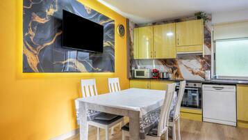 Een moderne keuken met gele kastjes, een flatscreen televisie aan de muur en een eettafel met stoelen.