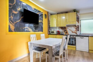 A modern kitchen with yellow cabinets, a flat-screen TV mounted on the wall, and a dining table with chairs.