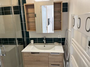Een badkamer met een witte wastafel, houten kastjes, een douchecabine met glazen wanden en een spiegel boven de wastafel.