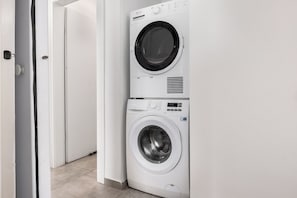 Voorweergave van een gestapelde wasmachine en droger in een gang.