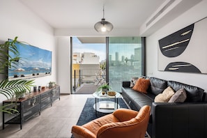 Een moderne woonkamer met een zwarte leren bank, een glazen salontafel en een groot stadsgezichtschilderij.