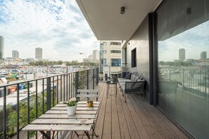 Un balcón con suelo de madera, una zona de estar con sofá y sillones, y una barandilla.