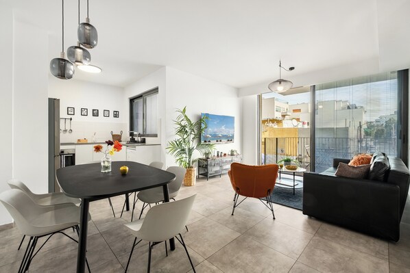 Una cocina moderna con armarios blancos, una zona de comedor con una mesa y sillas negras, y un ventanal con vistas a la ciudad.