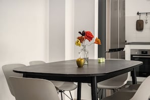 Een moderne eethoek met een ronde tafel, zes stoelen en een vaas met bloemen.