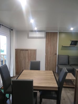 Ein Zimmer mit einem Holztisch, vier Stühlen, einem grauen Sofa, einem Holzschrank und einer Wand-Klimaanlage.