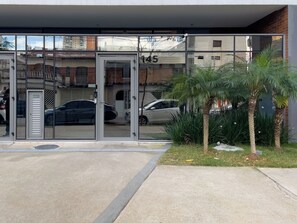 Entrada de un edificio con puertas de vidrio, el número '145' visible y automóviles estacionados.