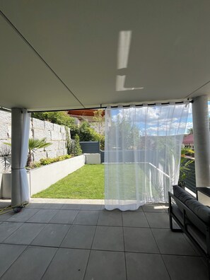 Ein überdachter Patio-Bereich mit Blick auf einen gepflegten Rasen und eine Steinsmauer.