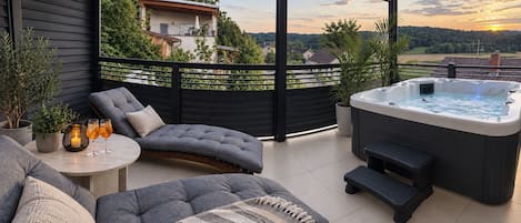 Un espacio moderno al aire libre con jacuzzi, asientos acolchados y vistas del paisaje circundante.