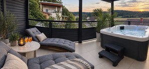Un espace extérieur moderne, aménagé pour se détendre, avec un jacuzzi, des sièges confortables et une vue sur le paysage environnant.