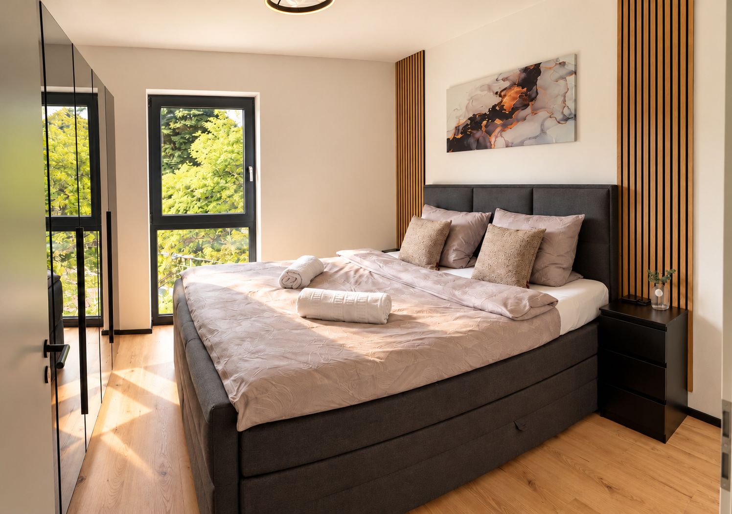 A modern bedroom with a large bed, a view of greenery through the window, and a minimalist decor.
