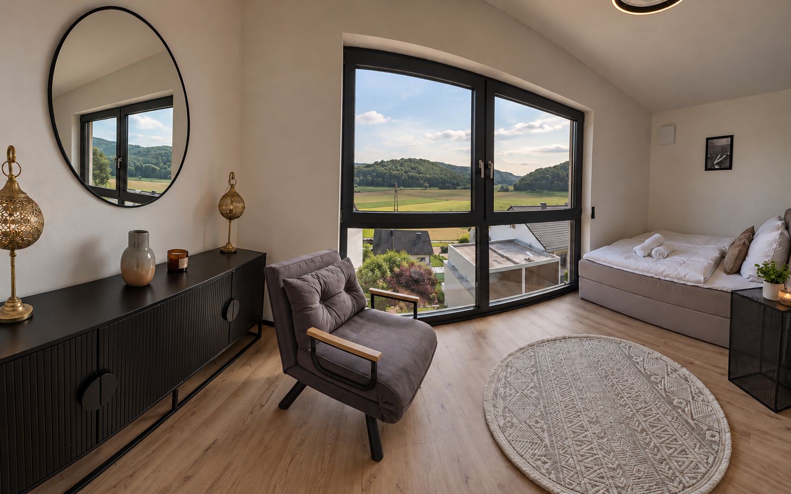 Un salon moderne comprenant un canapé, un fauteuil, une grande fenêtre donnant sur un paysage verdoyant, un tapis rond et une console noire agrémentée d’objets décoratifs.