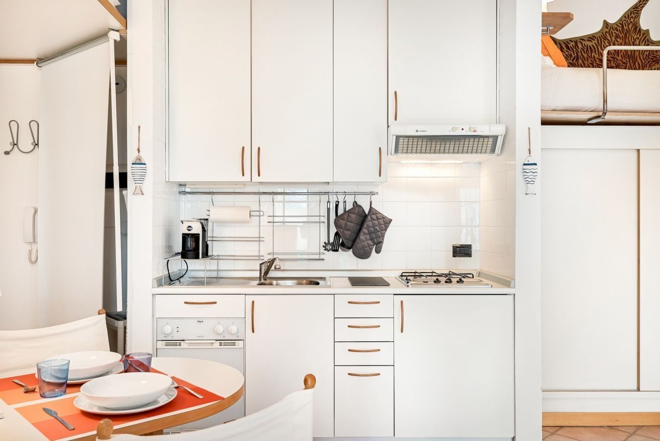 A compact kitchen with white cabinets, a stove, a sink, and a coffee maker.