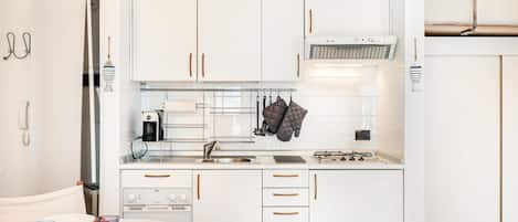 A compact kitchen with white cabinets, a stove, a sink, and a coffee maker.