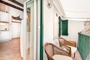 A room with a sliding glass door leading to a kitchen, a wicker chair, and a green shuttered window. - [LaCasaDiUgo] In the heart of Lerici+A/C (Lerici)
