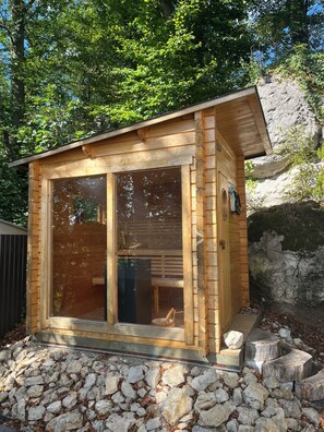 Una cabaña de madera con un amplio ventanal corredero, un porche pequeño y cimientos de piedra.