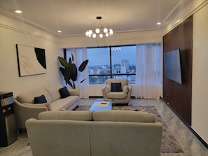 A modern living room with a sofa, armchair, and a coffee table. A large window offers a city view. - Staroot- The Platinum Place (Nairobi)