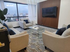 A modern living room with a sofa set, a coffee table, and a flat-screen TV mounted on a wooden wall. - Staroot- The Platinum Place (Nairobi)
