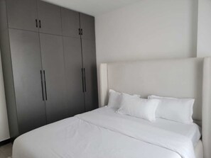 A bedroom with a large bed, a grey wardrobe, and a white headboard. - Staroot- The Platinum Place (Nairobi)