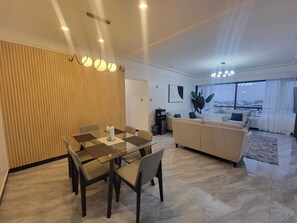 A modern living room with a sofa, a dining table with chairs, and a large window offering a city view. - Staroot- The Platinum Place (Nairobi)