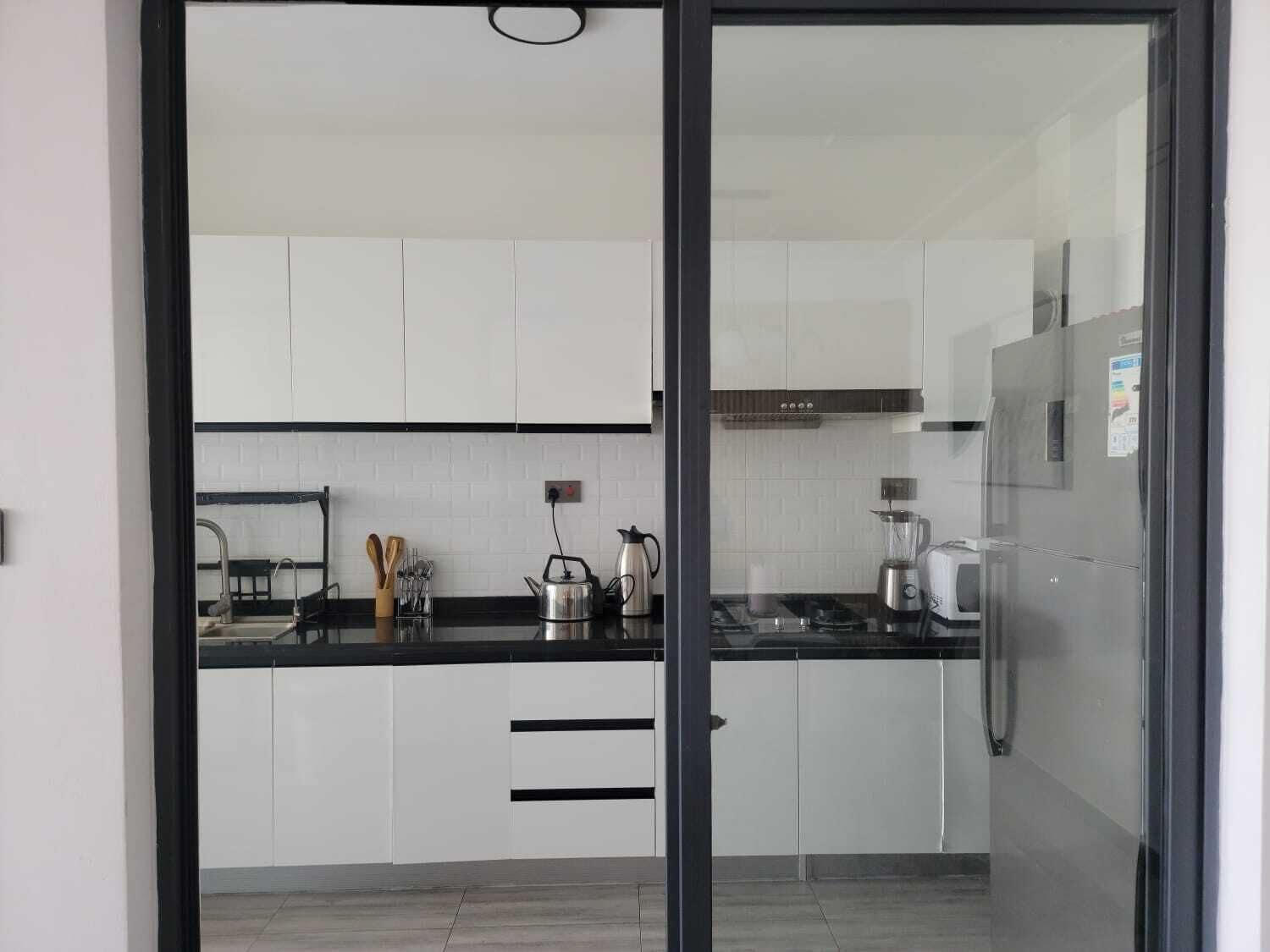 A modern kitchen with white cabinets, a black countertop, and stainless steel appliances including a kettle, toaster, and blender.