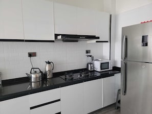 Una cuina moderna amb armaris blancs, una encimera negra, un refrigerador d'acer inoxidable, un microones, una olla elèctrica i una batedora.