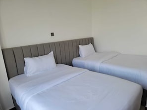 Duas camas de solteiro com cabeceiras cinzas e roupa de cama branca em um quarto.