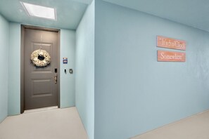 A hallway with a door, a number sign, and two signs on the wall. - Sister’s Paradise by AMI Locals (Bradenton)