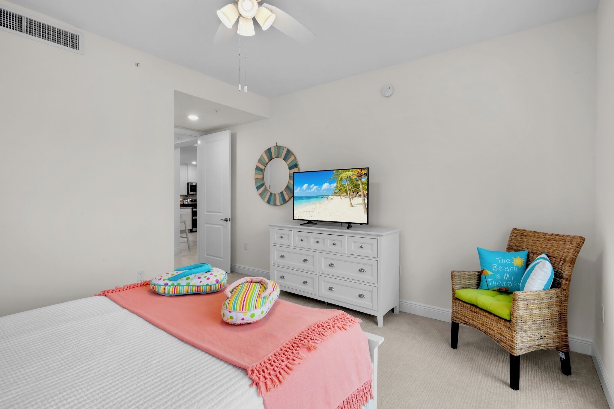 A bedroom with a bed, a television, a wicker chair, and a dresser.