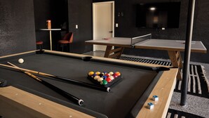 Ein Billardtisch mit Kugeln und Spielstöcken, ein Tischtennisständer und ein an der Wand befestigter Fernseher.