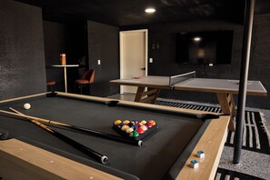 Ein Billardtisch mit Kugeln und Spielstöcken, ein Tischtennisständer und ein an der Wand befestigter Fernseher.